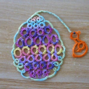 May include: A colorful crocheted egg bookmark with a small crocheted chick charm attached. The egg is a gradient of pink, purple, blue, green, and yellow.