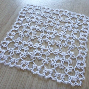 May include: White crocheted doily with a delicate floral pattern. The doily is square shaped and has a intricate design.