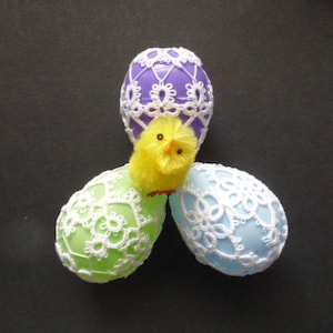 May include: Three crocheted Easter eggs, one purple, one light blue, and one light green, with a yellow chick in the center.
