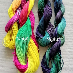 Può includere: Due bobine di filo da ricamo, una con un gradiente di giallo, verde e rosa, etichettata "Giorno", e l'altra con un gradiente di verde, blu e viola, etichettata "Notte".
