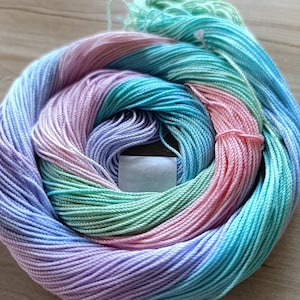 May include: A skein of multi-colored yarn in shades of pink, blue, and green. The yarn is wound into a circle and has a tag attached with the text "7" and "Fu".