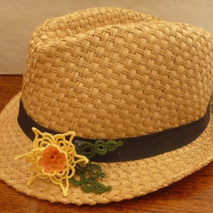 Puede incluir: Un sombrero de paja con una banda negra y una flor de ganchillo amarilla y verde.