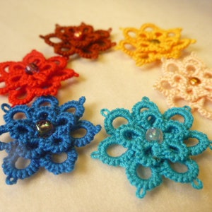 May include: Six crocheted flower designs with a bead in the centre. The flowers are in shades of red, orange, yellow, pink, and blue.