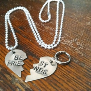May include: Two silver necklaces with heart-shaped pendants that say 'Be Friends' on them. The pendants are broken in half and fit together.