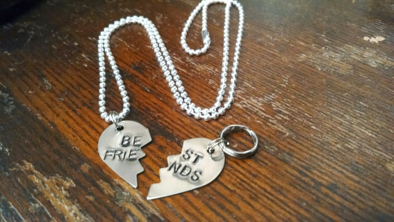 May include: Two silver necklaces with heart-shaped pendants that say 'Be Friends' on them. The pendants are broken in half and fit together.