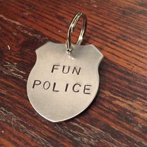 May include: A silver metal keychain shaped like a police badge with the words "FUN POLICE" engraved on it.