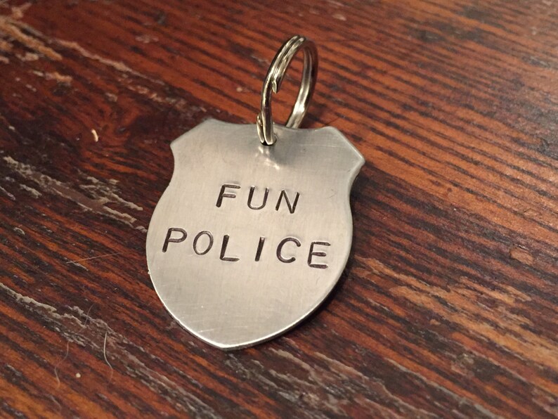 May include: A silver metal keychain shaped like a police badge with the words "FUN POLICE" engraved on it.