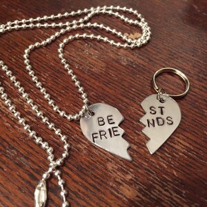 May include: Two silver heart-shaped pendants on a silver chain and a silver key chain. The pendants are broken in half and say 'Be Friends' on one and 'Best' on the other.