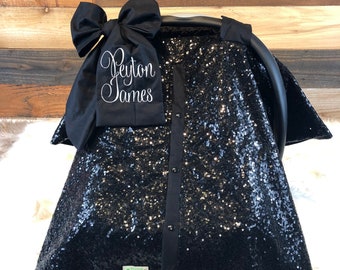 May include: Black sequin car seat cover with a black bow and a white embroidered name "Peyton James".