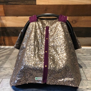 May include: A gold sequin car seat cover with purple trim and gold buttons. The cover has a small green tag with the text "Little Lambs" on it.