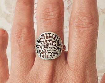 May include: A silver ring with a circular design featuring intricate Hebrew lettering.