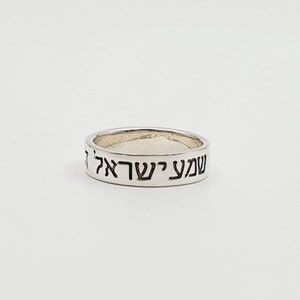 Puede incluir: Un anillo de plata con las palabras hebreas "Shema Yisrael" grabadas en la banda.
