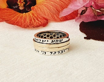 May include: Three silver rings stacked on top of each other. The top ring has a honeycomb pattern. The middle ring has the Hebrew word "עצבי" inscribed on it. The bottom ring has the Hebrew words "יהוה אלהי" inscribed on it.