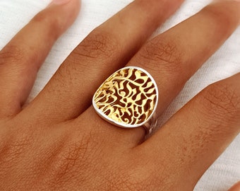May include: A silver ring with a gold-toned, oval-shaped top featuring a delicate, intricate, filigree design.