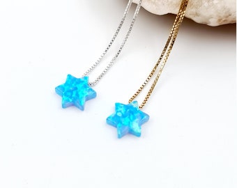 May include: Two necklaces with star-shaped pendants. One necklace has a silver chain, and the other has a gold chain. The star pendants are a bright blue color with a textured, opal-like appearance. The background is white with a light-colored stone.