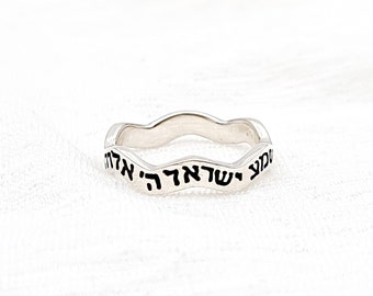 May include: A silver ring with a wavy band and Hebrew text inscribed around the band.