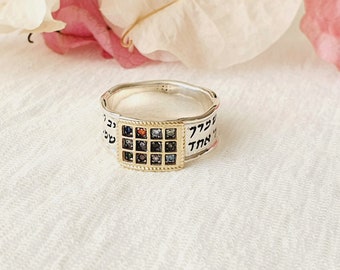 May include: A silver ring with a gold square inset featuring a grid of colorful gemstones. The ring is inscribed with Hebrew text on either side of the square.