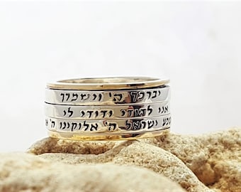 May include: A silver spinning ring with Hebrew text engraved on each band. The ring is made of multiple bands that spin around each other.