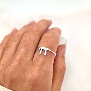 Puede incluir: Un anillo de plata con un diseño simple y delicado que presenta la letra hebrea Jai, símbolo de la vida.