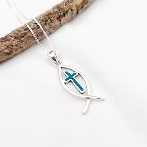 May include: A silver necklace with a turquoise blue enamel fish pendant featuring a cross inside. The pendant is on a silver chain.