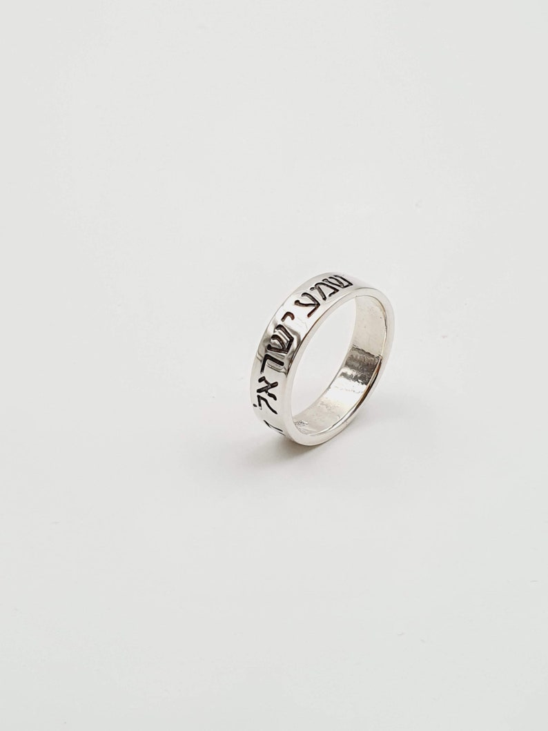 Puede incluir: Un anillo de plata con texto hebreo grabado alrededor de la banda.