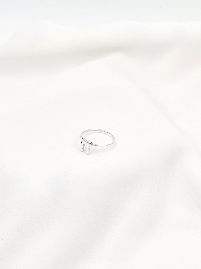 May include: A silver ring with a drip design. The ring is simple and modern.