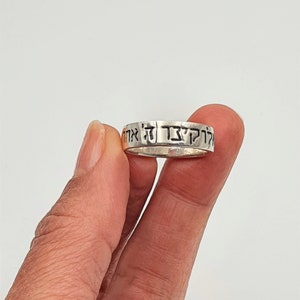 Puede incluir: Un anillo de plata con texto hebreo grabado alrededor de la banda. El texto dice "Kol HaKavod Le'at Ha'aretz".