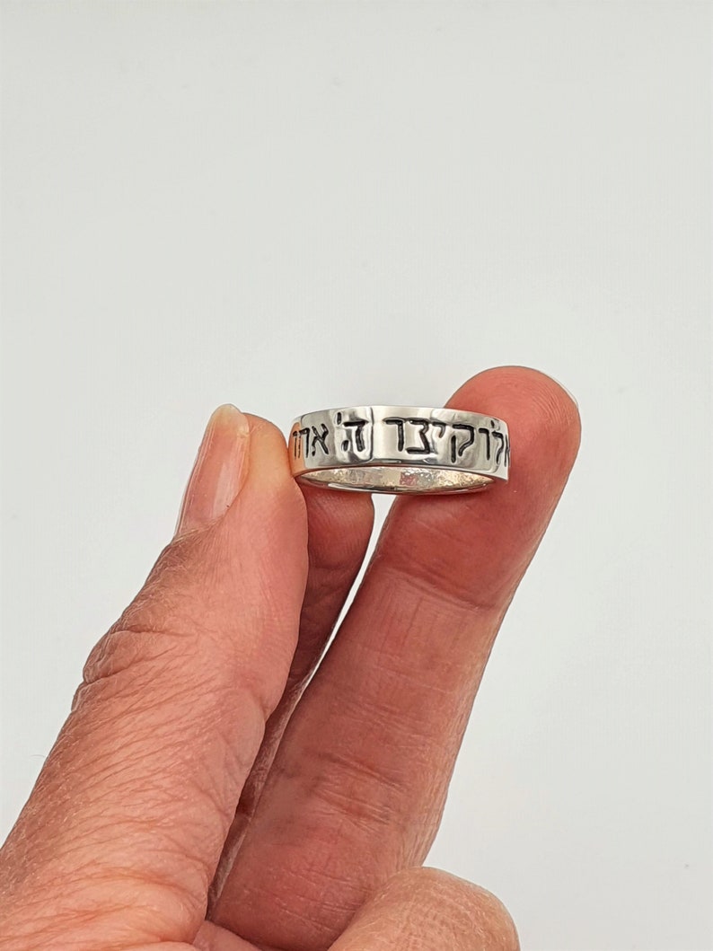 Puede incluir: Un anillo de plata con texto hebreo grabado alrededor de la banda. El texto dice "Kol HaKavod Le'at Ha'aretz".