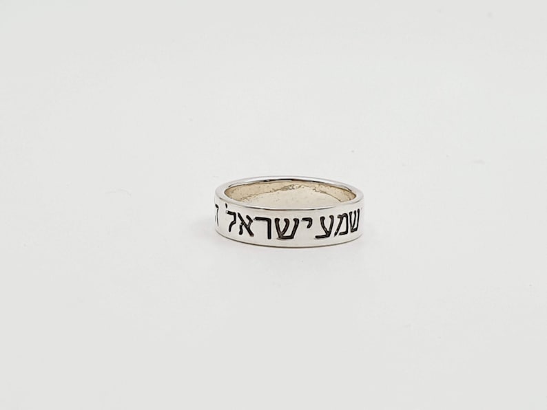 Puede incluir: Un anillo de plata con las palabras hebreas "Shema Yisrael" grabadas en la banda.
