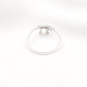 May include: A silver ring with a small, delicate design. The ring is shaped like the Hebrew letter 'Chai'.
