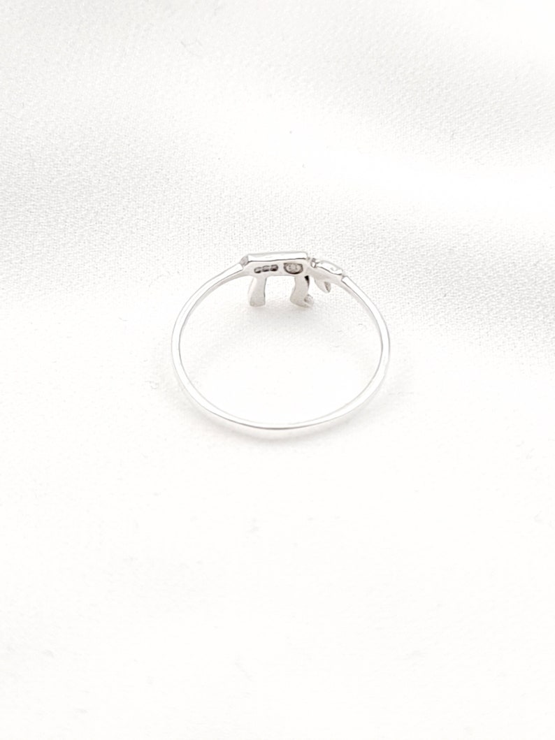 May include: A silver ring with a small, delicate design. The ring is shaped like the Hebrew letter 'Chai'.
