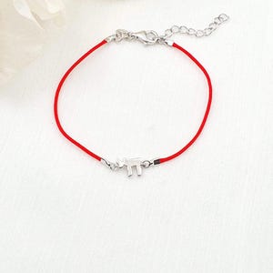 May include: Red string bracelet with a silver-colored charm in the shape of a rhino. The bracelet has a lobster clasp closure and an adjustable chain. The rhino charm is a small, detailed design.