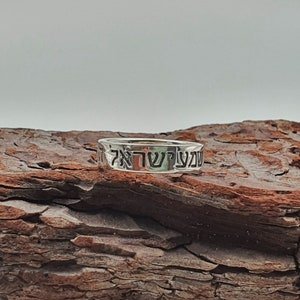 Puede incluir: Un anillo de plata con las palabras hebreas "עשה טוב" grabadas. El anillo est&aacute; apoyado en un trozo de madera desgastada.