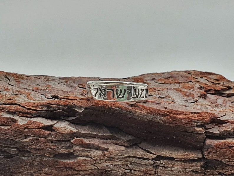 Puede incluir: Un anillo de plata con las palabras hebreas "עשה טוב" grabadas. El anillo est&aacute; apoyado en un trozo de madera desgastada.