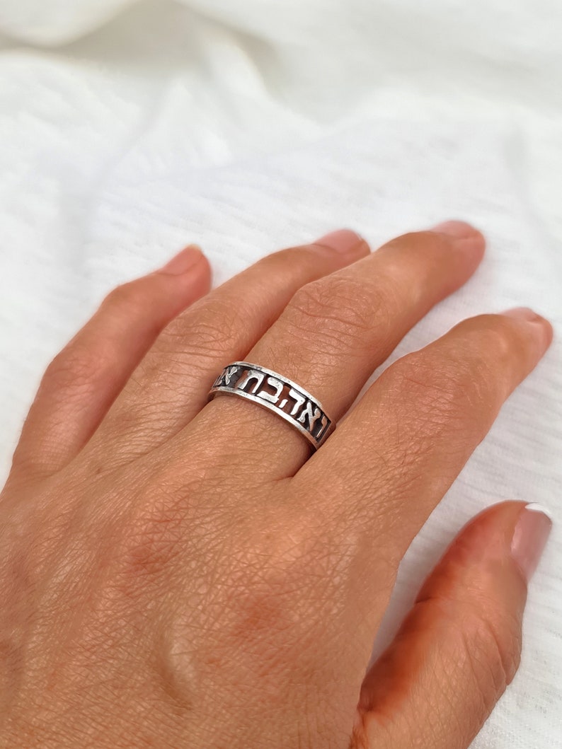 May include: A silver ring with Hebrew lettering. The ring is worn on a person's finger.