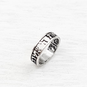 May include: A silver ring with Hebrew lettering engraved around the band.