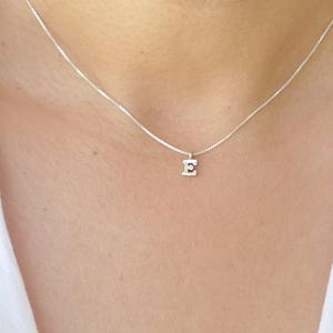 Puede incluir: Un collar de cadena de plata con un pequeño colgante de plata con la letra 'E'.