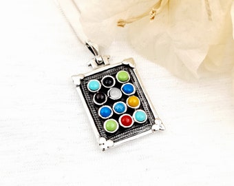 May include: A silver pendant necklace featuring a rectangular pendant with a matrix of colorful gemstones. The gemstones are various colors, including turquoise, black, white, green, blue, and red. The pendant has a detailed border and is suspended from a delicate silver chain.