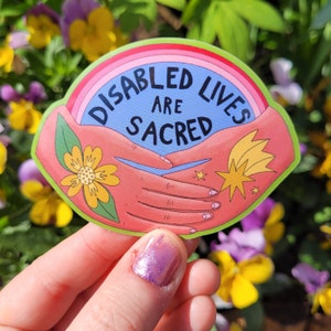 May include: A sticker with a rainbow background and two hands clasped together. The text reads "Disabled Lives Are Sacred".
