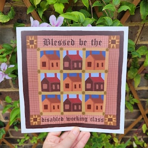 May include: Square print featuring a quilt-like design with nine houses in shades of brown, orange, and red. The text "Blessed be the" and "disabled working class" are displayed in a decorative font. The print has a brown border with star-like accents.
