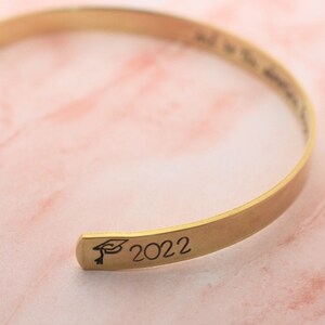 May include: Gold-toned bangle bracelet with an engraved graduation cap and the year 2022.