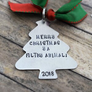 May include: A silver Christmas tree bauble with the text "Merry Christmas ya Filthy Animal! 2018" on it. The bauble is attached to a red and green ribbon.