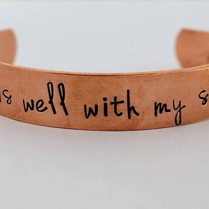 May include: Copper bracelet with the inscription "It is well with my soul".