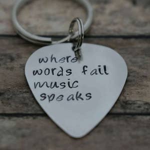 May include: Silver guitar pick keychain with the text "where words fail music speaks" engraved on it.