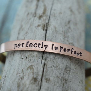 May include: A copper bracelet with the words "perfectly imperfect" engraved on it.