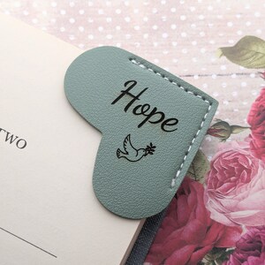 May include: A green leather heart-shaped bookmark with the word "Hope" and a dove with an olive branch engraved on it.
