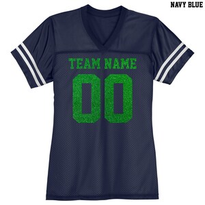Puede incluir: Jersey azul marino con rayas blancas en las mangas. El jersey tiene cuello en V y el texto "TEAM NAME" y el n&uacute;mero "00" en purpurina verde.