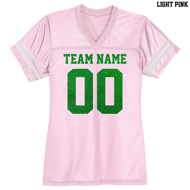 Puede incluir: Jersey rosa claro con rayas blancas en las mangas. El jersey tiene un n&uacute;mero "00" de purpurina verde y el texto "TEAM NAME" en la parte delantera.