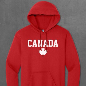 Peut inclure: Sweat-shirt à capuche rouge avec le mot "CANADA" et une feuille d'érable blanche imprimée sur le devant.