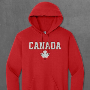 May include: Red hooded sweatshirt with the word "CANADA" and a silver glitter maple leaf on the front.